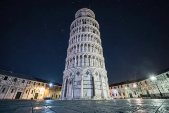 La tour de Pise photographiée de nuit en contre-plongée, façade en marbre blanc se découpant sur un ciel nocturne étoilé